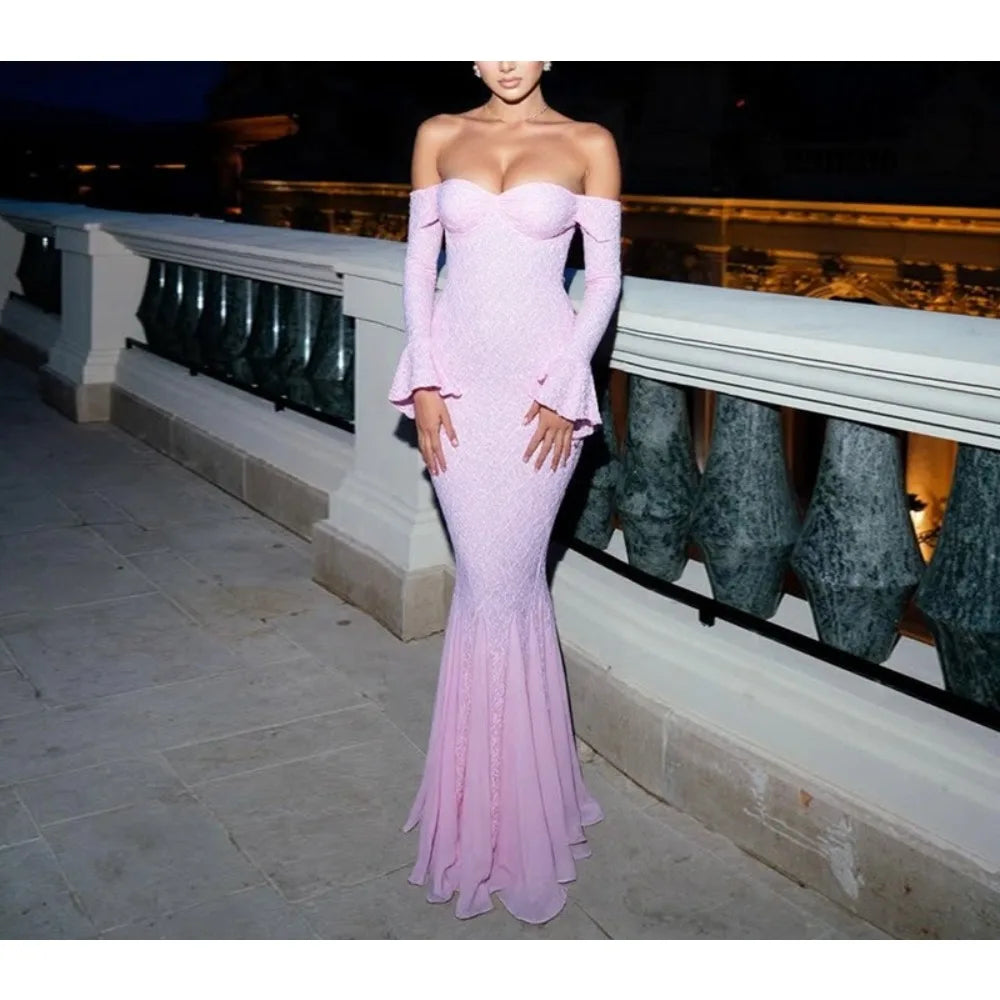 Woman wearing a pink off-shoulder gown standing on a balcony at night.