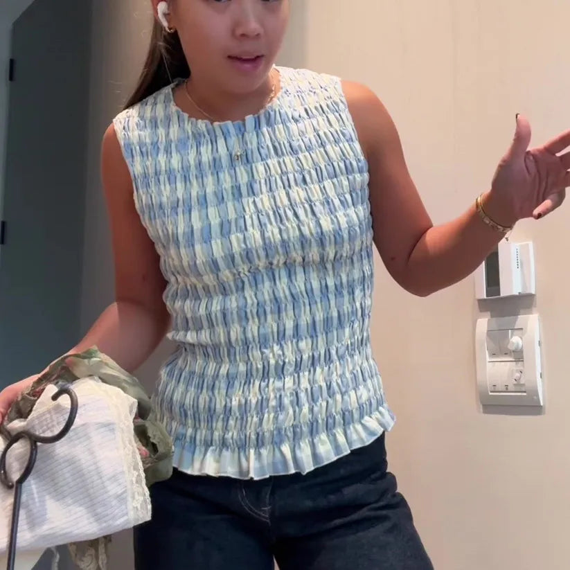 Woman wearing a blue and white patterned sleeveless top, holding a white cloth.