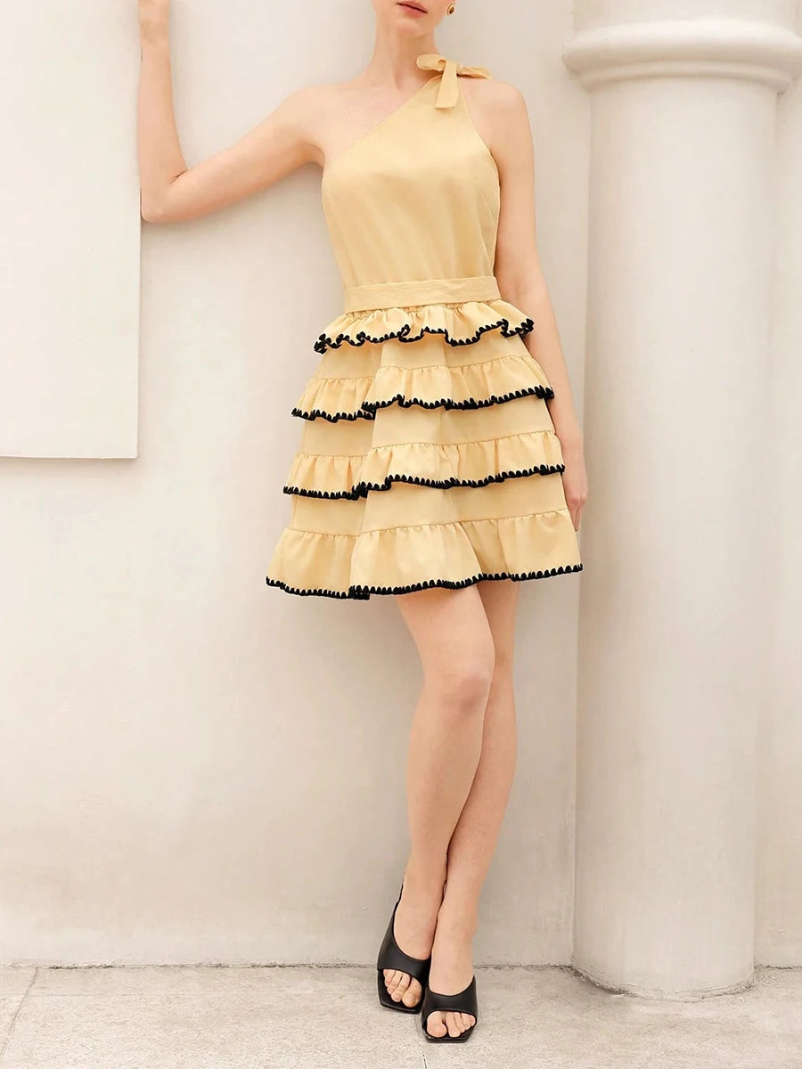 Woman wearing a yellow dress with black trim against a white wall.