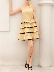 Woman wearing a yellow dress with black trim against a white wall.