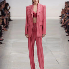 Model wearing a pink pinstripe suit on a runway with an audience.