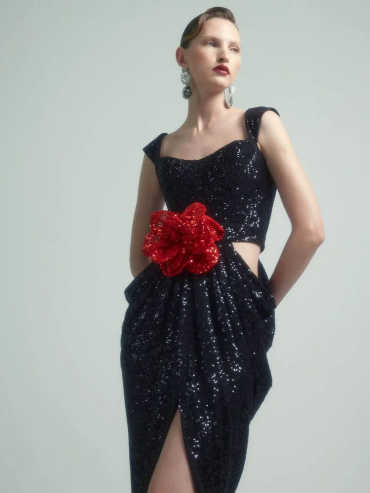 Black sequin dress with a red floral accent on a model against a gray background