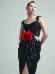 Black sequin dress with a red floral accent on a model against a gray background
