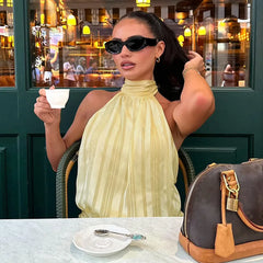 Woman in a yellow dress sitting at an outdoor cafe, holding a cup.