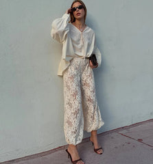 Woman wearing a white blouse and lace pants against a light blue wall.