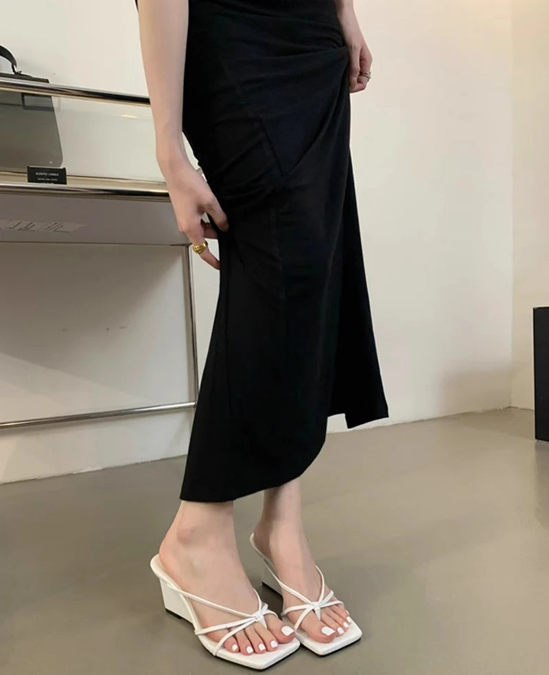 Person wearing a black dress and white sandals in an indoor setting