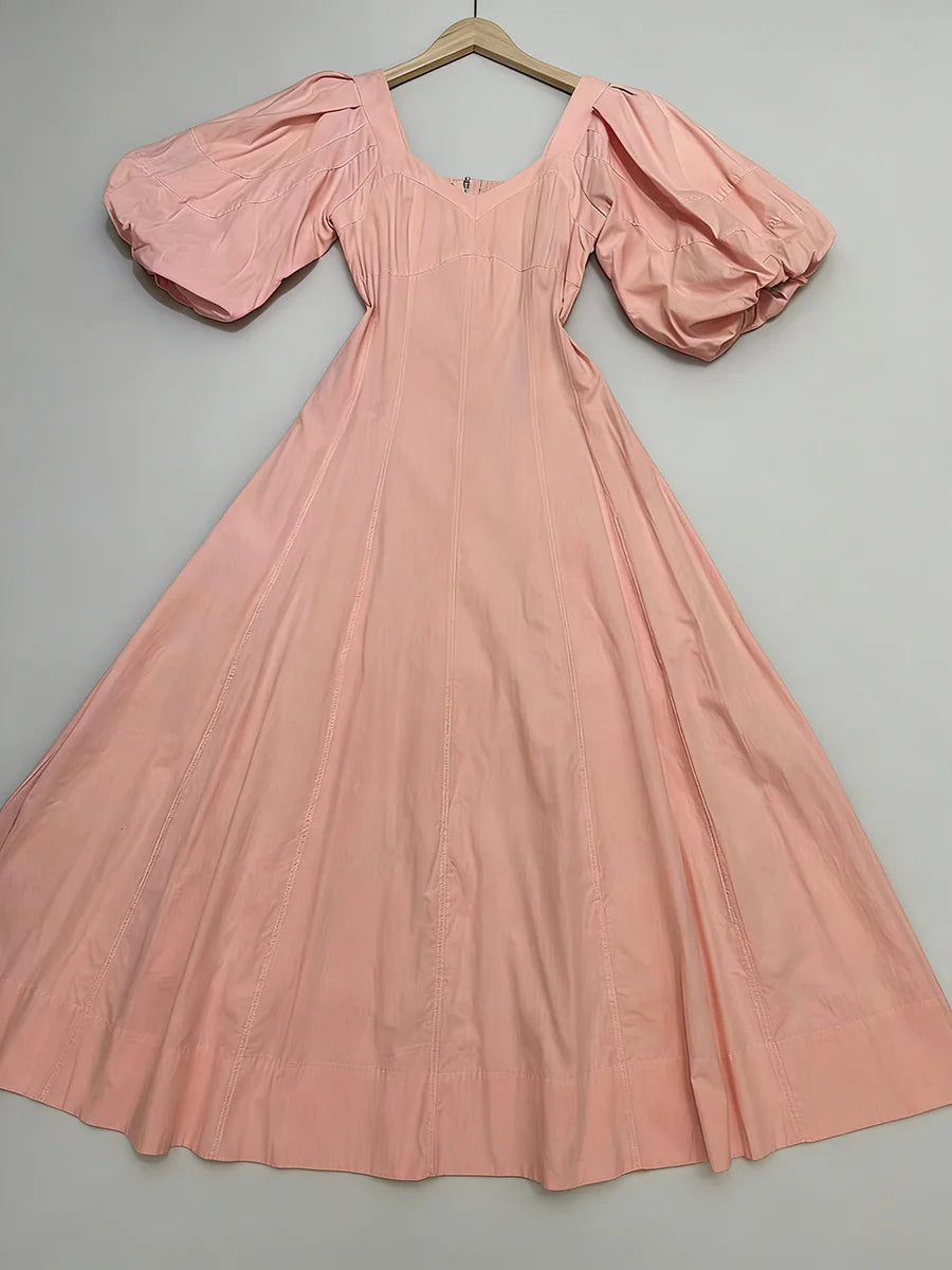 Pink dress with puffed sleeves on a hanger against a gray background