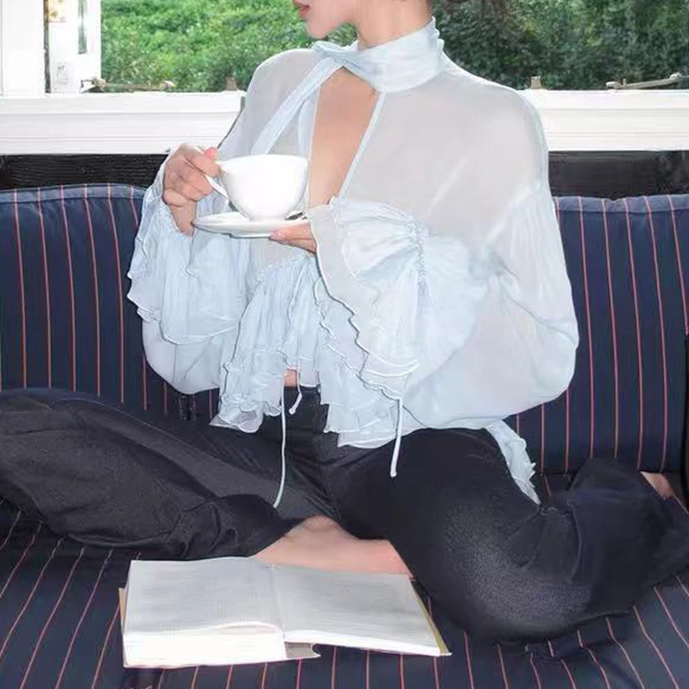Woman wearing a sheer ruffled halter blouse, holding a teacup and saucer.