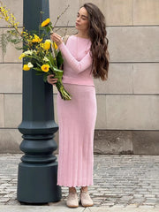 Woman in a pink outfit holding flowers against a stone wall.