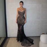 Woman wearing a black lace strapless gown against a neutral wall.