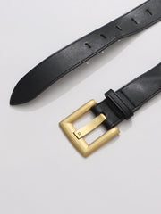 Black leather belt with a gold buckle on a light gray background