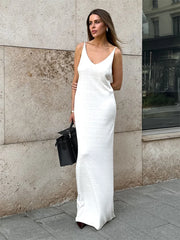 Woman in a white slip dress standing against a textured wall.