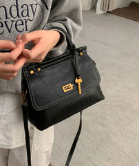 Person holding a black handbag with gold accents on a light gray floor.