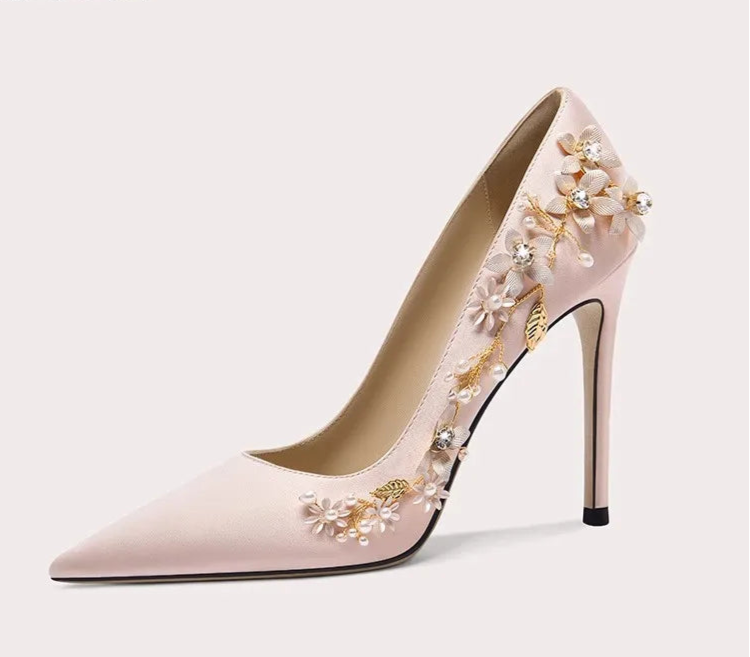 Pink high-heeled shoe with floral embellishments on a light gray background