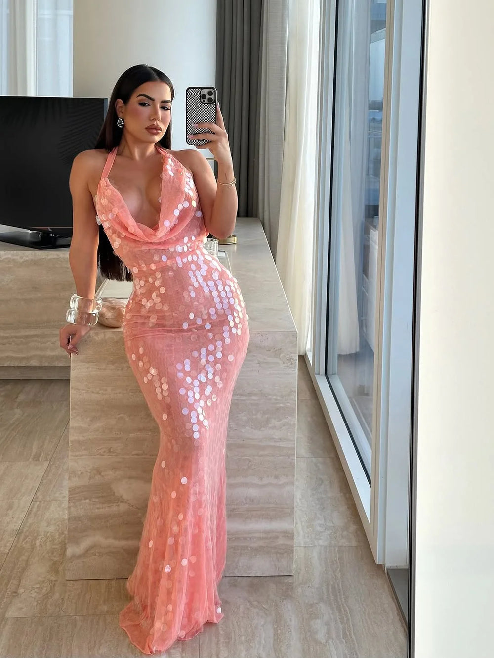 Woman in a pink sequin dress taking a mirror selfie in a modern interior setting.