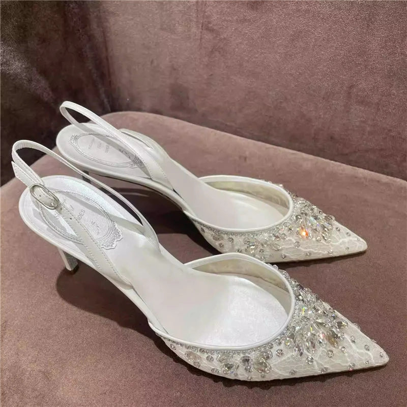 White high-heeled shoes with crystal embellishments on a brown surface