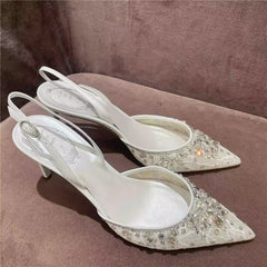 White high-heeled shoes with crystal embellishments on a brown surface