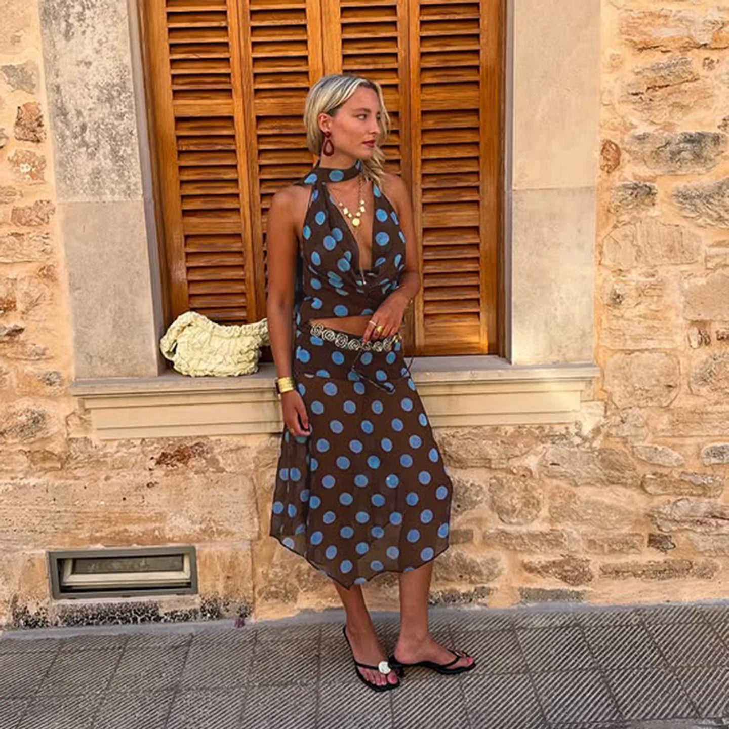 Woman in a polka dot dress standing in front of a stone wall with wooden shutters.