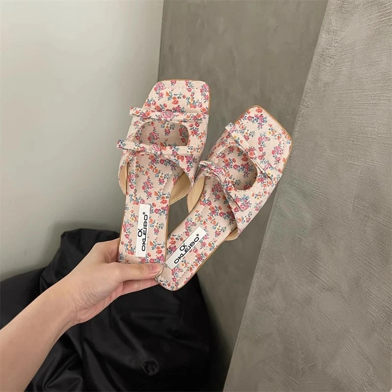 Floral high-heeled shoes held by a hand against a neutral background
