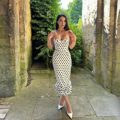 Woman in a polka dot dress standing in a stone pathway with greenery.