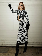 Woman wearing a black and white floral outfit against a white brick wall.