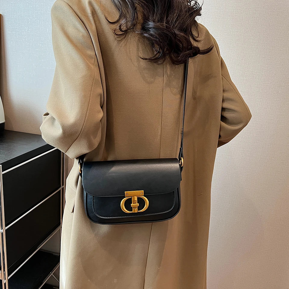 Person wearing a beige coat with a black handbag featuring a gold clasp.