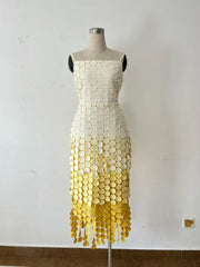 Mannequin wearing a dress with a white top and yellow fringe bottom against a plain wall.