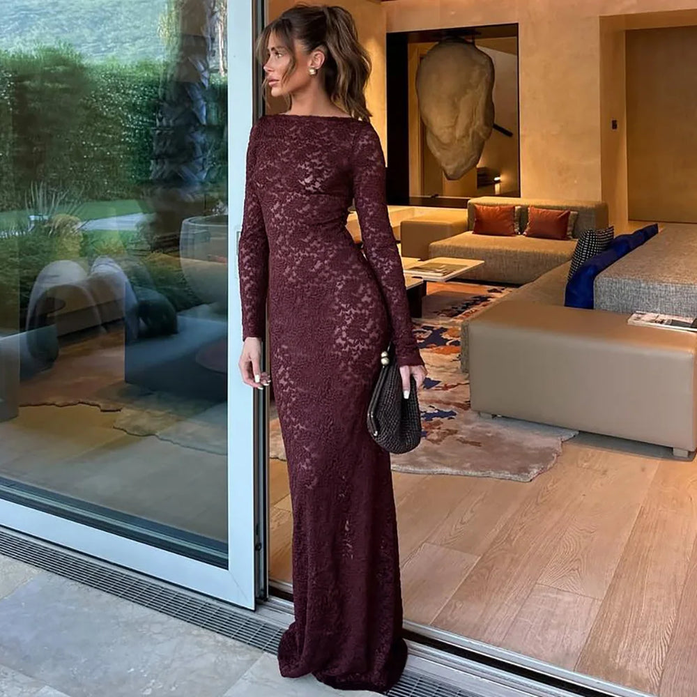 Woman in a burgundy lace dress standing by a glass door in a modern living room.