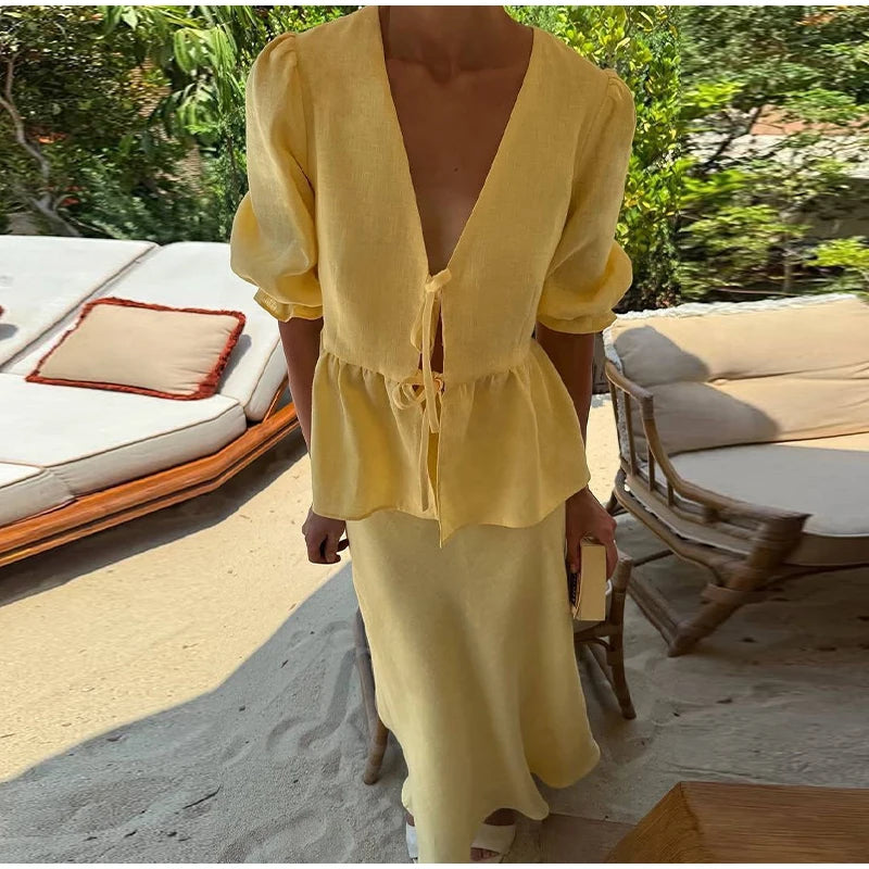 Person wearing a yellow outfit standing on a sandy beach with outdoor furniture in the background.