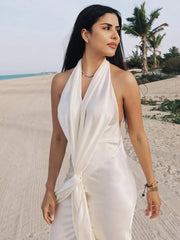 Woman in a white dress standing on a sandy beach with palm trees in the background