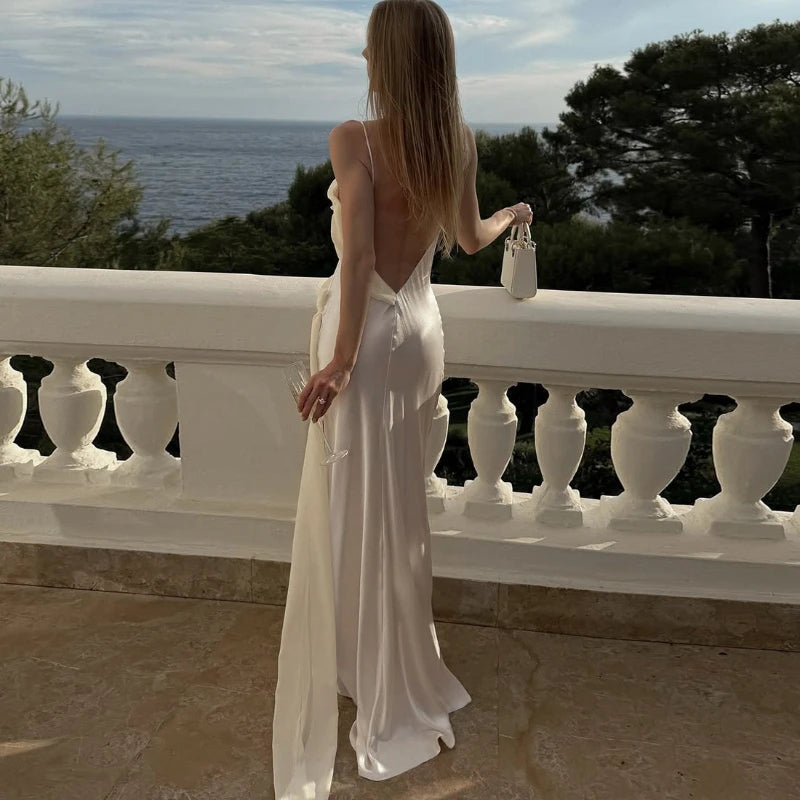 Woman in a white dress standing on a balcony overlooking the ocean.