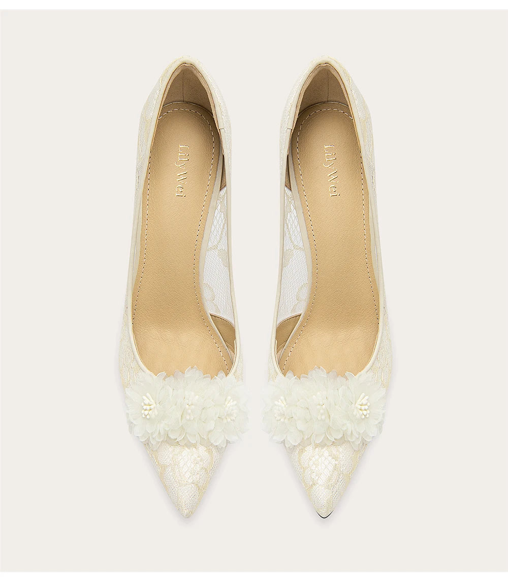 Pair of white pointed-toe shoes with floral details on a light gray background