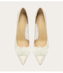 Pair of white pointed-toe shoes with floral details on a light gray background