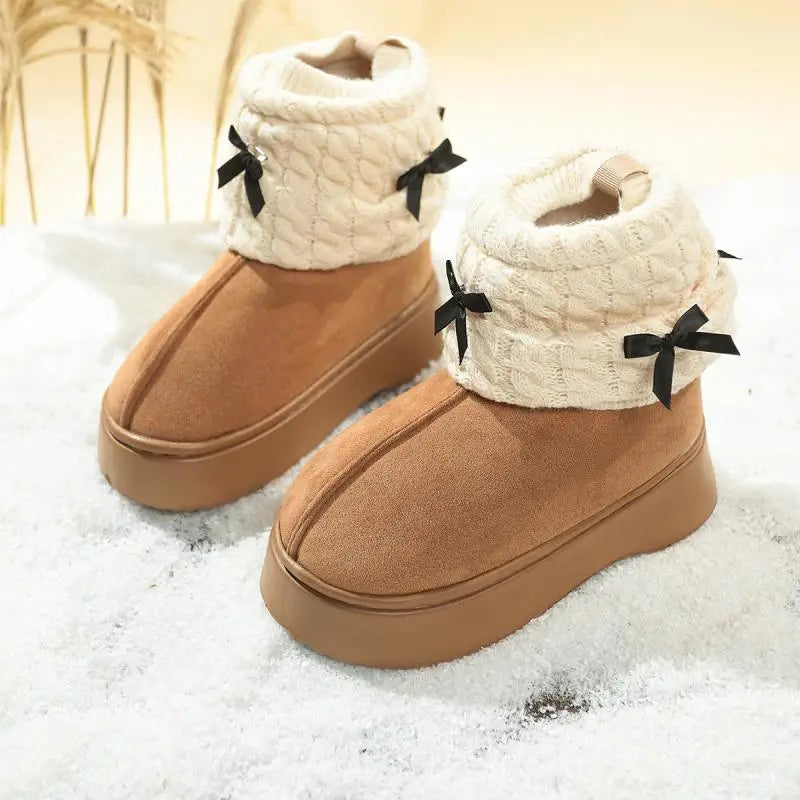 Pair of tan boots with white cuffs and black bows on a snowy background