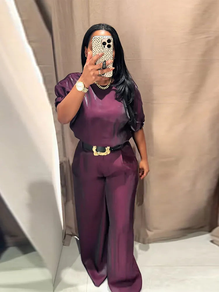 Person wearing a purple outfit with a belt, standing against a neutral background.