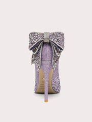 Purple glittery high-heeled shoe with a large bow on a light gray background