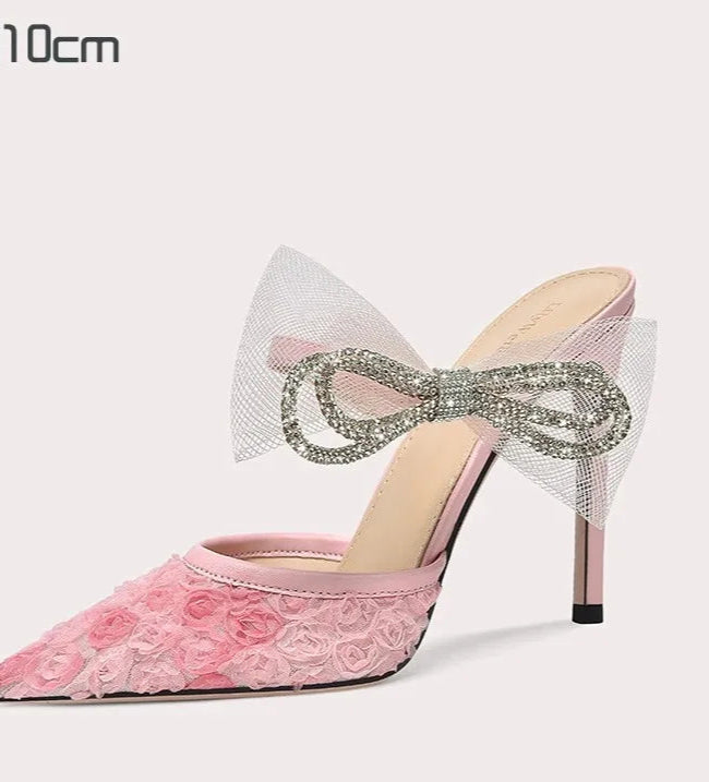 Pink high-heeled shoe with floral design and decorative bow on a white background