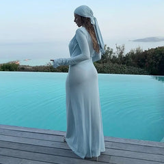 Woman in a white dress standing by an infinity pool with a scenic view.