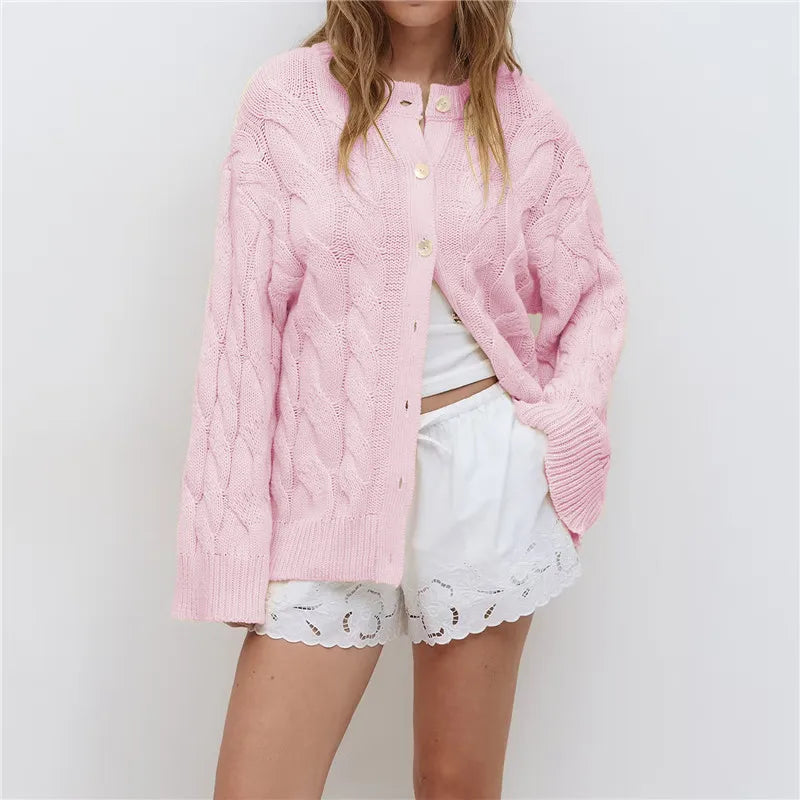 Person wearing a pink knitted cardigan over a white outfit with lace details on a plain background