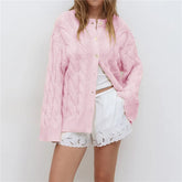 Person wearing a pink knitted cardigan over a white outfit with lace details on a plain background