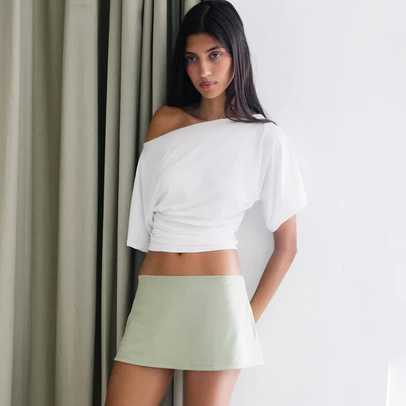 Woman wearing a white off-shoulder top and light green skirt against a neutral background