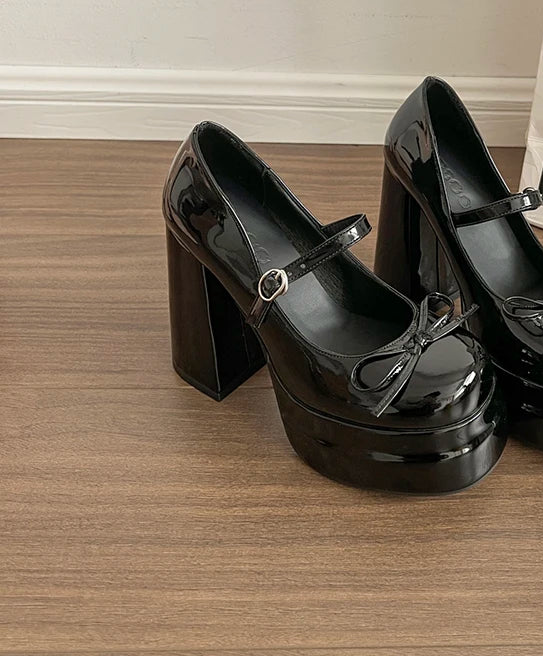 Black platform shoes on a wooden floor with a white wall in the background.