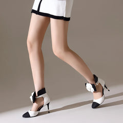 White high-heeled shoes with black accents worn by a person on a neutral background
