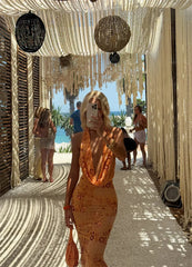 Woman in a floral dress standing under decorative string lights with a beach setting in the background.