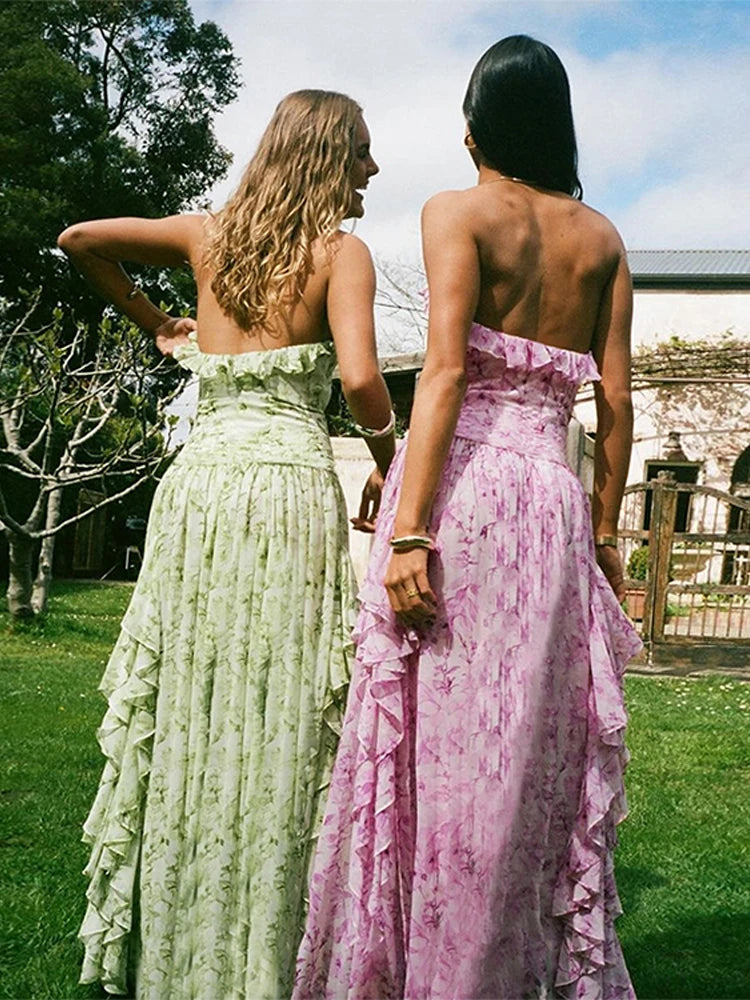 Two women in floral dresses standing outdoors with trees and a house in the background.