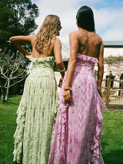 Two women in floral dresses standing outdoors with trees and a house in the background.
