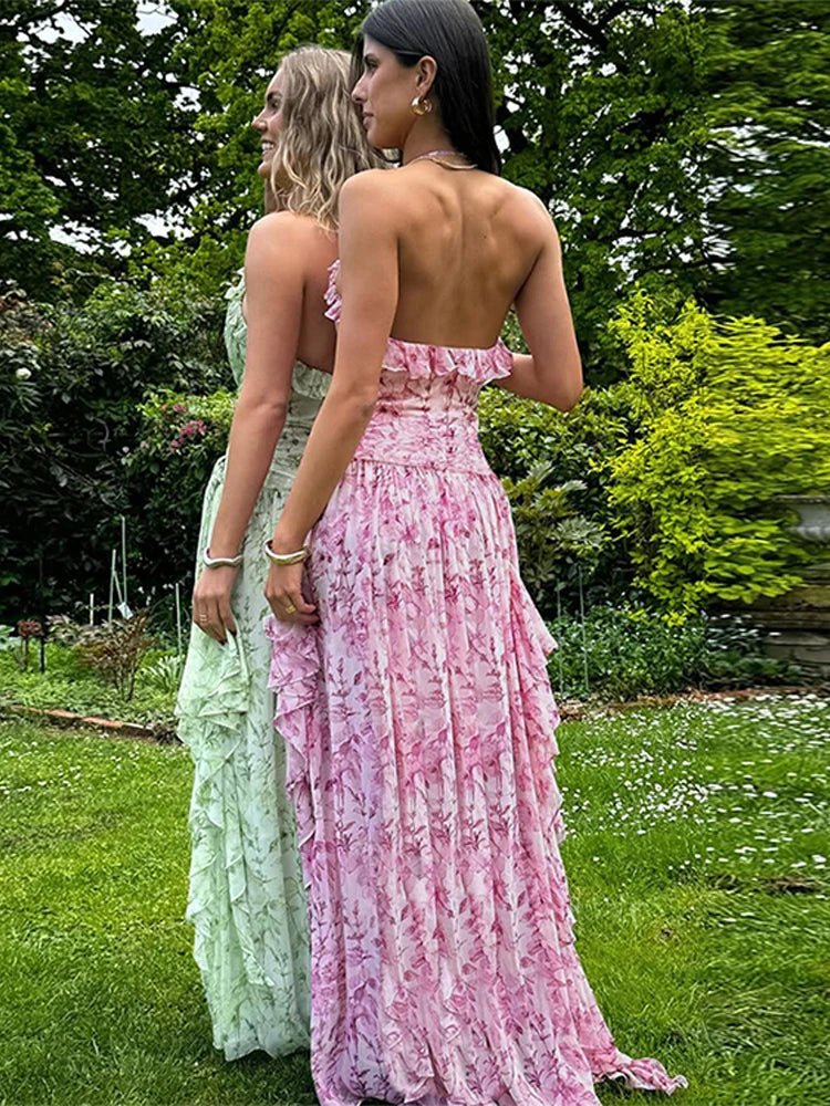 Two women in formal dresses standing outdoors with greenery in the background