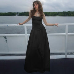 Woman in a black dress standing on a boat with water and trees in the background