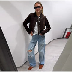 Person wearing a brown jacket, white shirt, and ripped blue jeans in a modern interior setting.