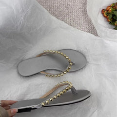 Pair of silver flat embellished flip flops on white tissue paper.